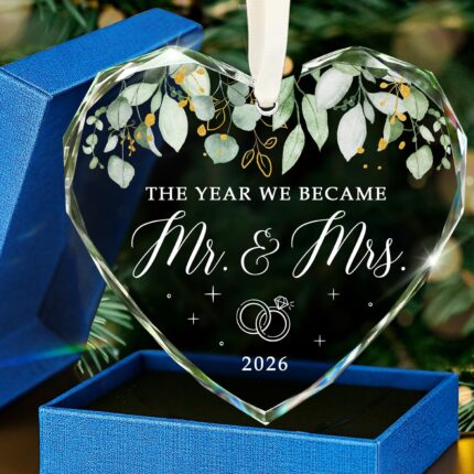 HEXMOZ Mr & Mrs 2026 heart-shaped glass ornament in a navy blue gift box with an ivory ribbon, hanging.