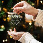 HEXMOZ Mr & Mrs 2026 heart-shaped glass ornament in a navy blue gift box with an ivory ribbon, hanging.