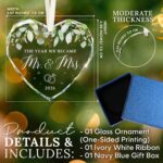 HEXMOZ Mr & Mrs 2026 heart-shaped glass ornament in a navy blue gift box with an ivory ribbon, hanging.