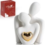 A white ceramic abstract statue depicting two figures hugging, with a golden heart detail, placed on a surface.