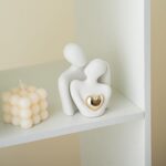 A white ceramic abstract statue depicting two figures hugging, with a golden heart detail, placed on a surface.
