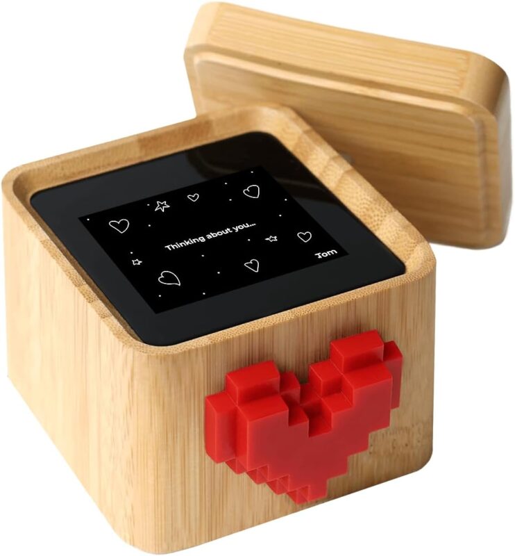 A black and white Lovebox device with a spinning red pixel heart on top, displaying a message on its screen.