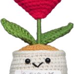 A small, red crochet doll with a flower head and a heart-shaped body, resting on a flat surface.