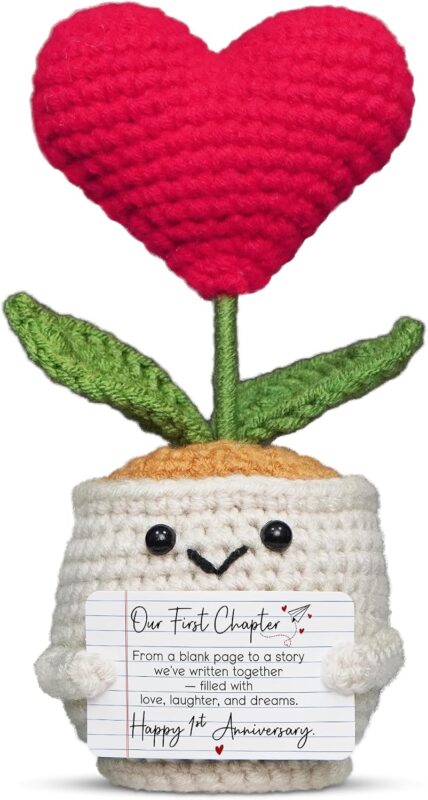 A small, red crochet doll with a flower head and a heart-shaped body, resting on a flat surface.