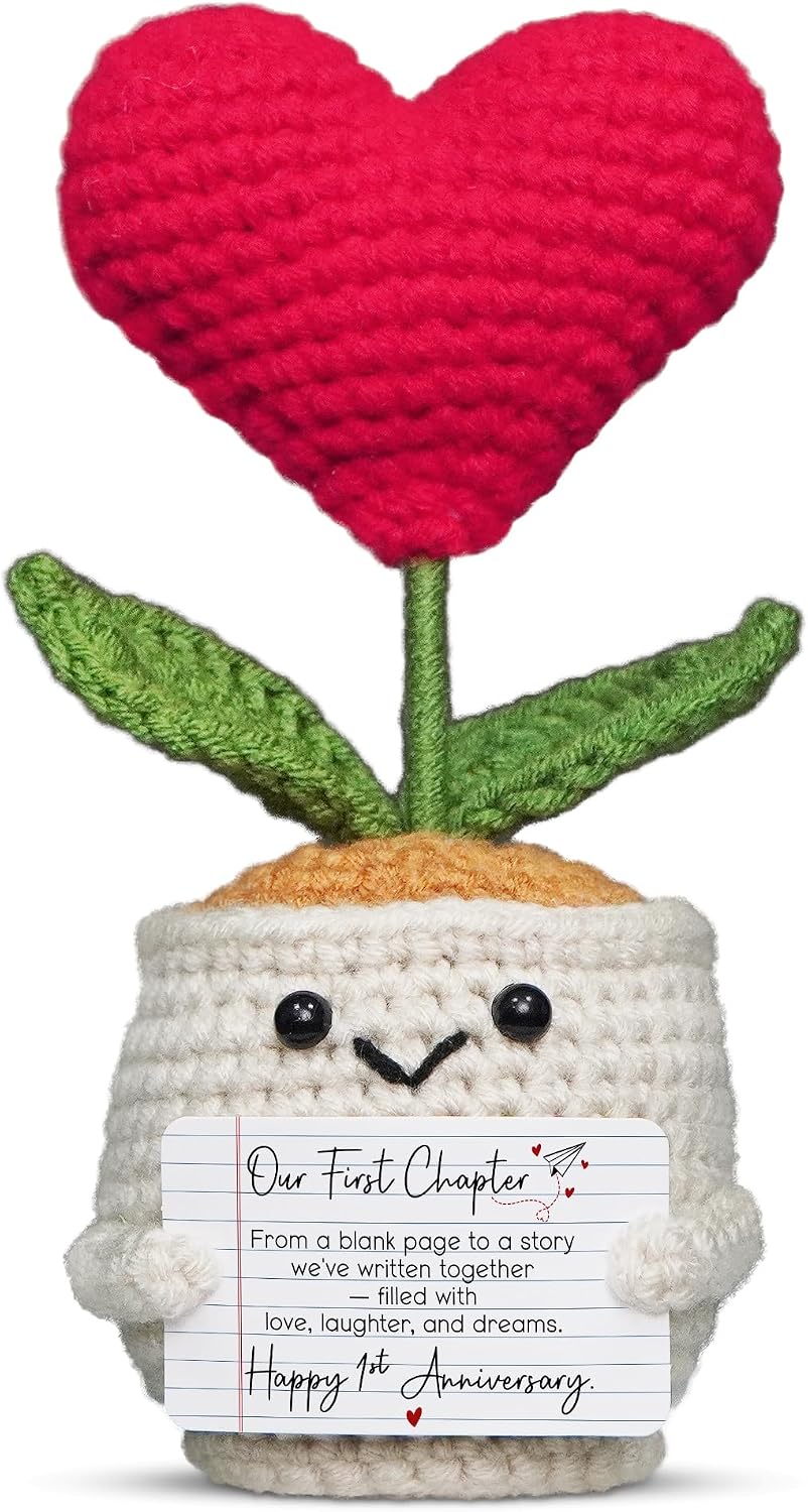 A small, red crochet doll with a flower head and a heart-shaped body, resting on a flat surface.