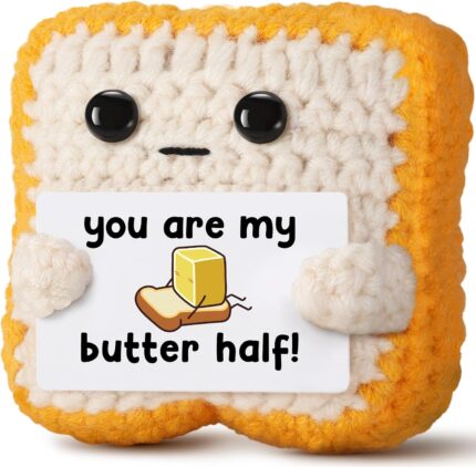 Close-up of a small, square, light brown crochet toast plush with embroidered eyes and a red heart, holding a white banner th
